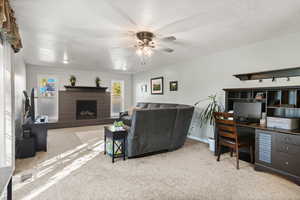 Living room featuring a textured ceiling, light carpet, ceiling fan, and a fireplace