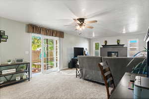 Living room featuring a textured ceiling, plenty of natural light, carpet, a glass covered fireplace, and ceiling fan