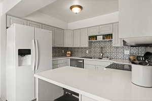 Kitchen with white fridge with ice dispenser, a peninsula, backsplash, quartz counters, and open shelves
