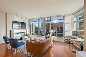 Living room featuring plenty of natural light, wood finished floors, a glass covered fireplace, and rail lighting