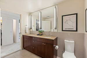 Full bathroom with double vanity, light tile patterned floors, light colored carpet, and a spacious closet