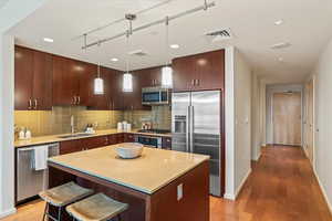 Kitchen with appliances with stainless steel finishes, tasteful backsplash, a kitchen breakfast bar, a center island, and pendant lighting