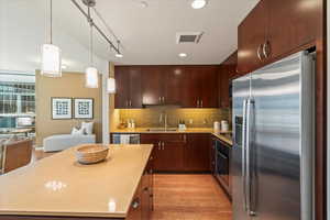 Kitchen featuring stainless steel appliances, light wood-type flooring, backsplash, pendant lighting, and open floor plan