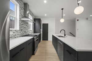 Kitchen featuring dark cabinetry, modern cabinets, pendant lighting, appliances with stainless steel finishes, and wall chimney exhaust hood
