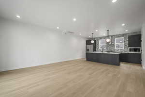 Kitchen featuring open floor plan, a center island with sink, pendant lighting, light countertops, and light wood-style flooring