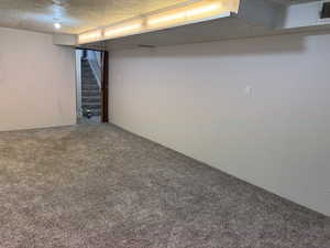 Finished below grade area featuring carpet, a textured ceiling, and stairway