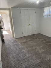 Unfurnished bedroom featuring a textured ceiling, dark carpet, a closet, and multiple windows