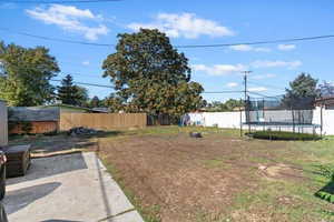 Fenced backyard featuring a trampoline and a playground