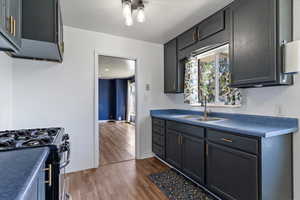 Kitchen with dark wood finished floors, dark countertops, black range with gas cooktop, and gray cabinets