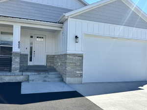 Doorway to property with board and batten siding, covered porch, stone siding, and driveway