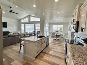Kitchen featuring a kitchen bar, an island with sink, stainless steel appliances, light stone counters, and a textured ceiling