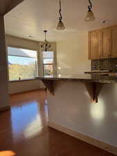 Kitchen with a breakfast bar, pendant lighting, dark stone countertops, decorative backsplash, and dark wood-style floors