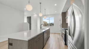 Images shown are of a similar completed unit. Kitchen with appliances with stainless steel finishes, light wood-style floors, modern cabinets, hanging light fixtures, and a spacious island