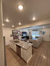 Kitchen with light stone counters, white cabinetry, open floor plan, an island with sink, and a textured ceiling