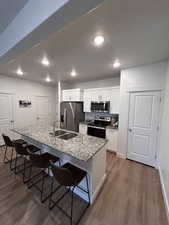 Kitchen with a breakfast bar, light stone countertops, dark wood-style flooring, stainless steel appliances, and a kitchen island with sink