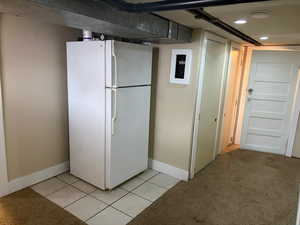 Finished basement with freestanding refrigerator, light tile patterned floors, and light carpet