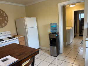 Kitchen with light tile patterned floors, white appliances, light countertops, crown molding, and washer and dryer