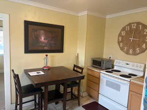 Kitchen featuring white electric stove, crown molding, light tile patterned floors, and light countertops