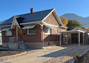 View of front of house featuring driveway, brick siding, a carport, and a chimney