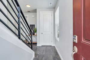 Foyer featuring stairway, LVP flooring, door straight ahead is a coat closet. Door to the left of the table is a bedroom w ensuite bathroom.