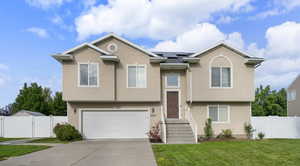 Bi-level home with roof mounted solar panels, stucco siding, a garage, driveway, and a gate