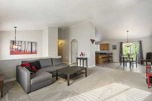 Living room with a chandelier, light colored carpet, arched walkways, and high vaulted ceiling