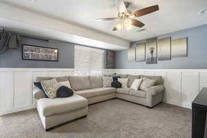 Carpeted basement living area with a decorative wall, a wainscoted wall, a ceiling fan, and a textured ceiling
