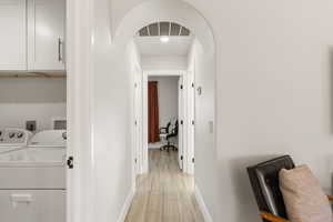 Hall featuring arched walkways, light wood finished floors, and separate washer and dryer