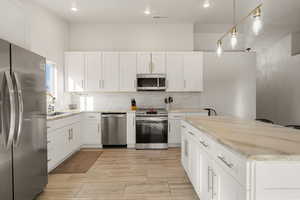 Kitchen with hanging light fixtures, appliances with stainless steel finishes, white cabinets, backsplash, and recessed lighting