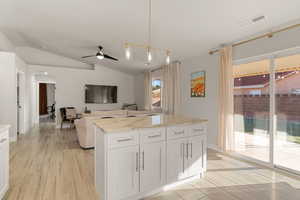 Kitchen featuring hanging light fixtures, arched walkways, white cabinets, light stone counters, and wood finish floors