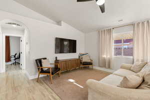 Living area featuring arched walkways, lofted ceiling, light wood-style flooring, and a ceiling fan