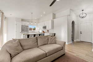 Living area with arched walkways, a ceiling fan, light wood-style flooring, and vaulted ceiling