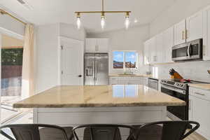 Kitchen with stainless steel appliances, white cabinets, decorative backsplash, hanging light fixtures, and light stone counters