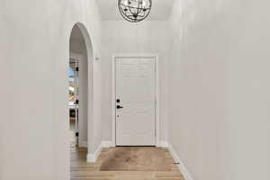 Foyer entrance featuring arched walkways, light wood-type flooring, and a chandelier