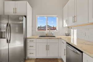 Kitchen featuring stainless steel appliances, white cabinets, light stone counters, backsplash, and light wood finished floors