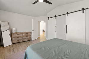 Bedroom featuring lofted ceiling, light wood-style floors, a barn door, ceiling fan, and arched walkways