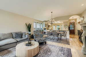 Living room featuring light wood-style flooring, vaulted ceiling, a chandelier, and a fireplace