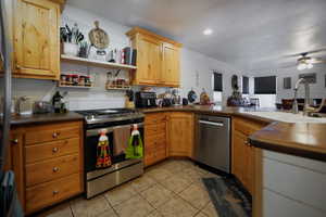 Kitchen with stainless steel appliances, dark countertops, light tile patterned floors, ceiling fan, and a peninsula