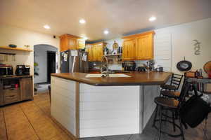 Kitchen featuring open shelves, dark countertops, arched walkways, a peninsula, and appliances with stainless steel finishes