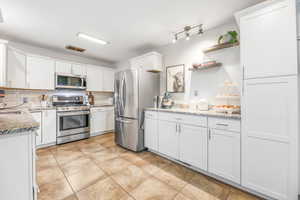 Kitchen with stainless steel appliances, white cabinetry, open shelves, and decorative backsplash