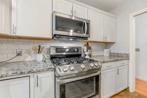 Kitchen featuring stainless steel appliances, backsplash, and white cabinets
