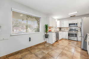 Kitchen featuring backsplash, white cabinetry, stainless steel appliances, and light stone counters