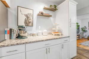 Kitchen with white cabinetry, open shelves, and light stone counters