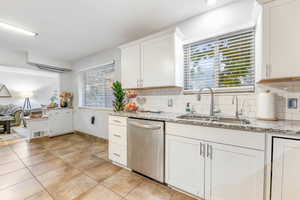 Kitchen featuring plenty of natural light, light stone countertops, white cabinets, and dishwasher