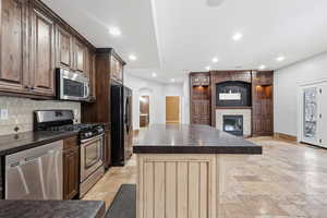 Second kitchen with appliances with center island, arched walkways, dark brown cabinetry, and stone tile flooring.  Perfect for multi gen living or rental