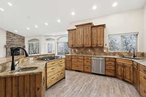 Kitchen featuring light stone countertops, decorative backsplash, stainless steel appliances, light wood-style flooring.