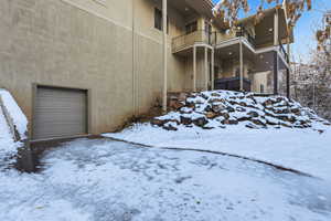 Snow covered property featuring stucco siding, a balcony, and entrance to the large lower level garage