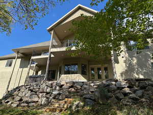 Back of property featuring a balcony, a shingled roof, a patio area, stucco siding, and doors