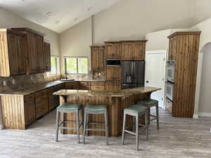 Kitchen featuring a kitchen bar, stainless steel and black appliances, high vaulted ceiling, dark stone counters, and a center island