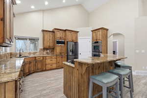 Kitchen with brown cabinetry, tasteful backsplash, a kitchen island with sink, high vaulted ceiling, and light wood-type flooring